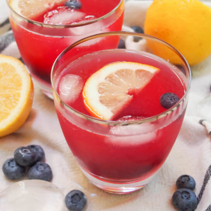 glass of blueberry lemonade with lemons and blueberry around