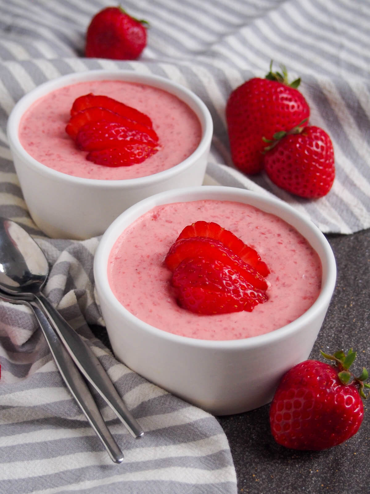 two dishes of finished dish with strawberries around dishes and spoons to side