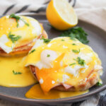 eggs Benedict with yolk running into sauce and lemon behind