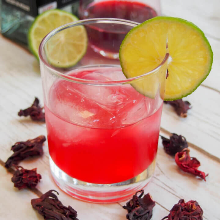 glass of hibiscus mezcal sour garnished with slice of lime