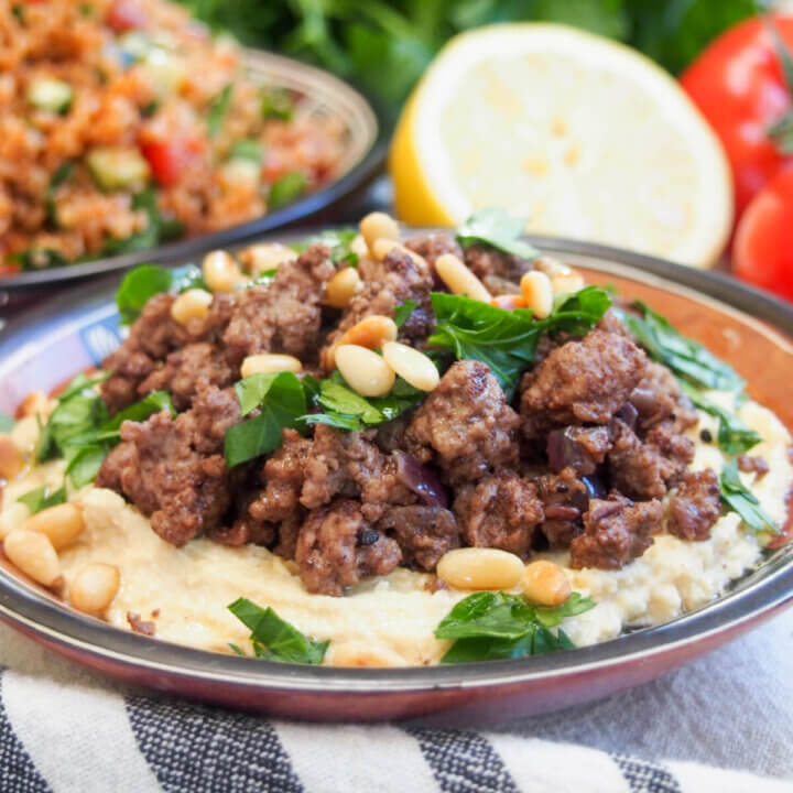 dish of hummus with lamb topped with parsley and pine nuts