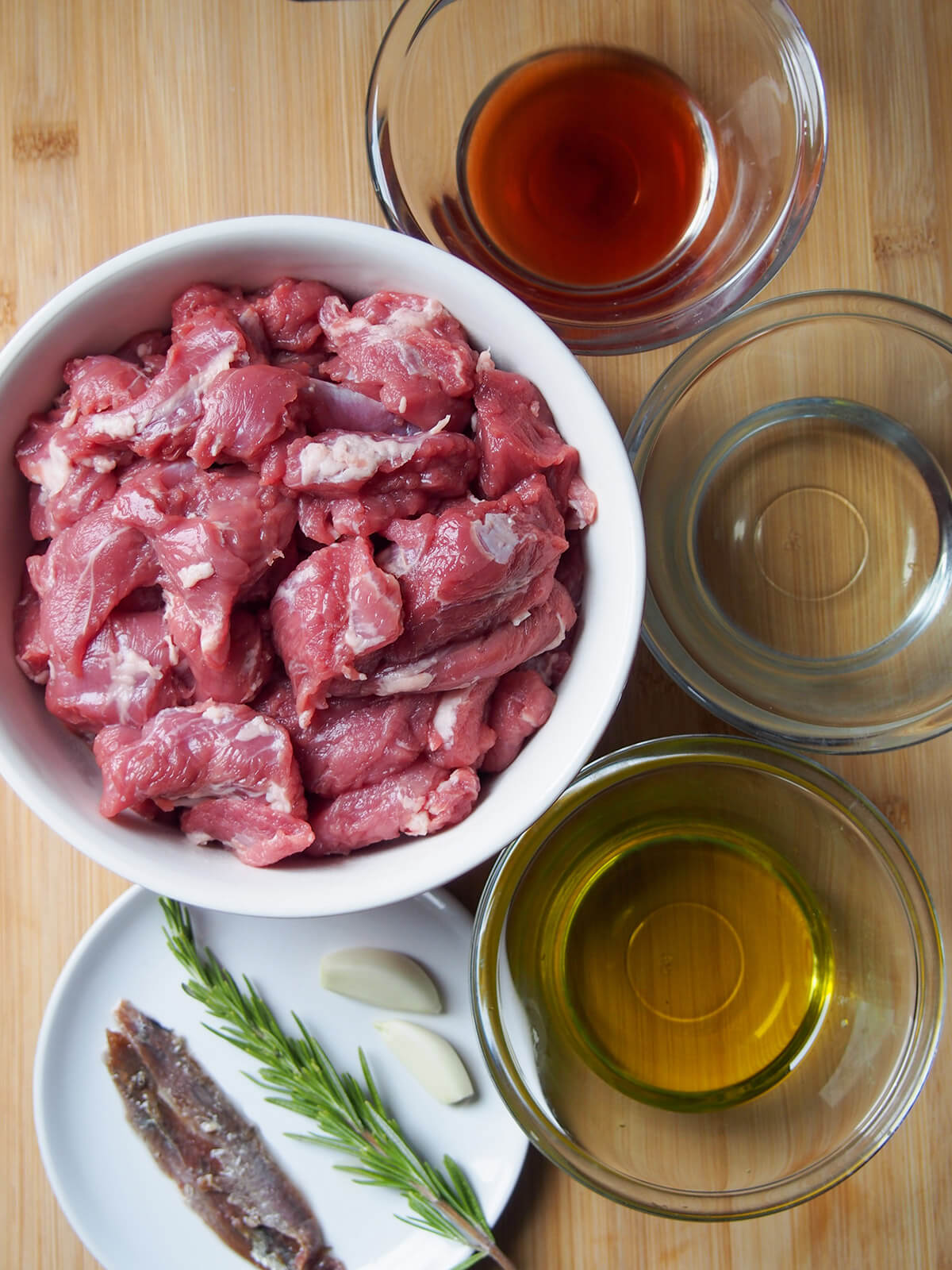 bowl of diced lamb, smaller bowls with wine, vinegar and oil and plate with anchovies, rosemary and garlic fr Roman lamb stew bowl of diced lamb, smaller bowls with wine, vinegar and oil and plate with anchovies, rosemary and garlic