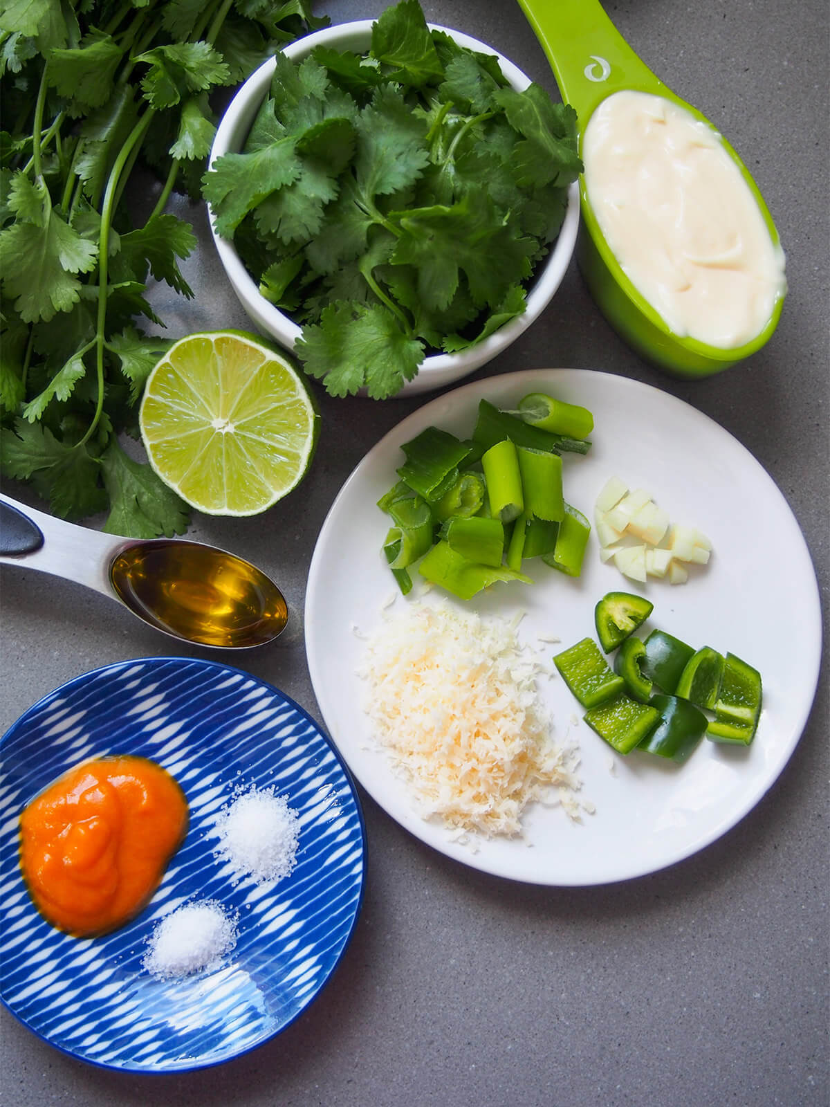 aji verde (Peruvian green sauce) ingredients cilantro in bowl, measure with mayonnaise, plates with chili, cheese, garlic and other ingredients and lime to side