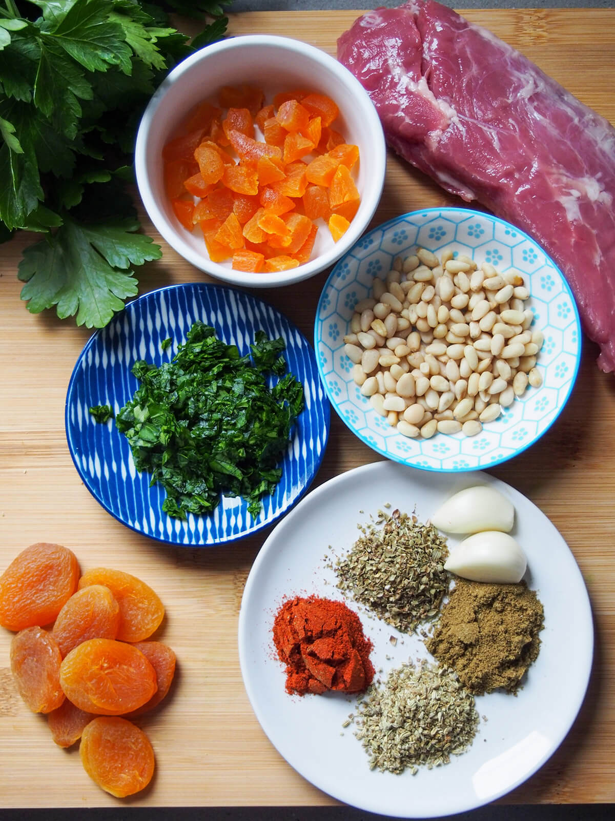 spices for rub on plate, parsley, pine nuts and apricots in dishes and pork to side