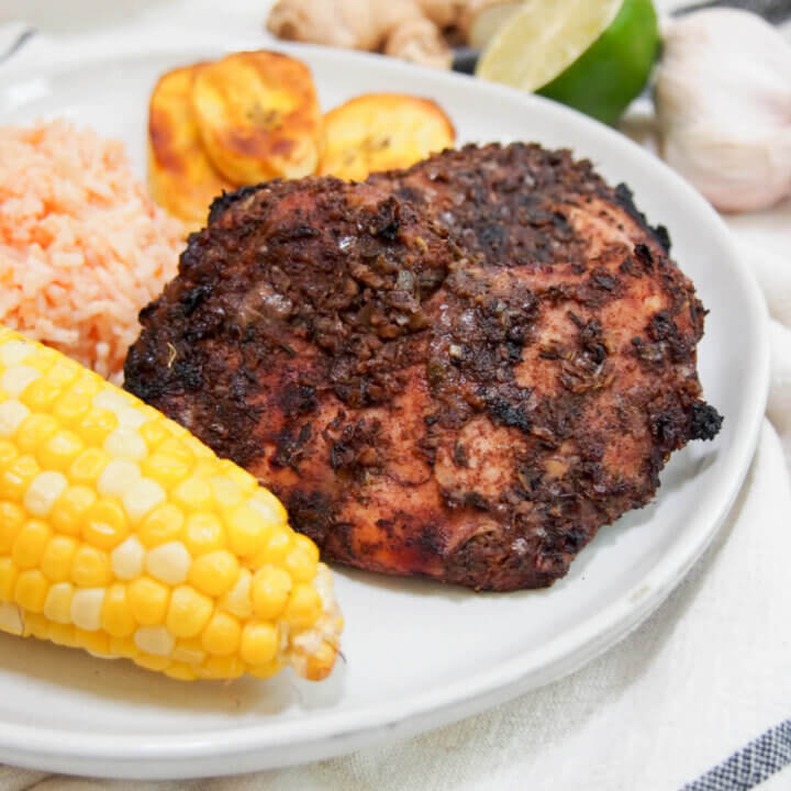 Jamaican jerk chicken on plate with corn in front and plantain behind