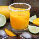glass of mango margarita with lime and mango pieces to side
