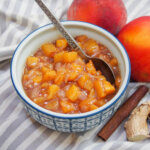 small bowl of peach chutney with peaches to side