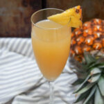 glass of pineapple mimosa with pineapple behind