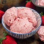 scoops of roasted strawberry ice cream in bowl with strawberries to side
