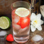 glass of st germain gin and tonic with lime to one side and flower to other