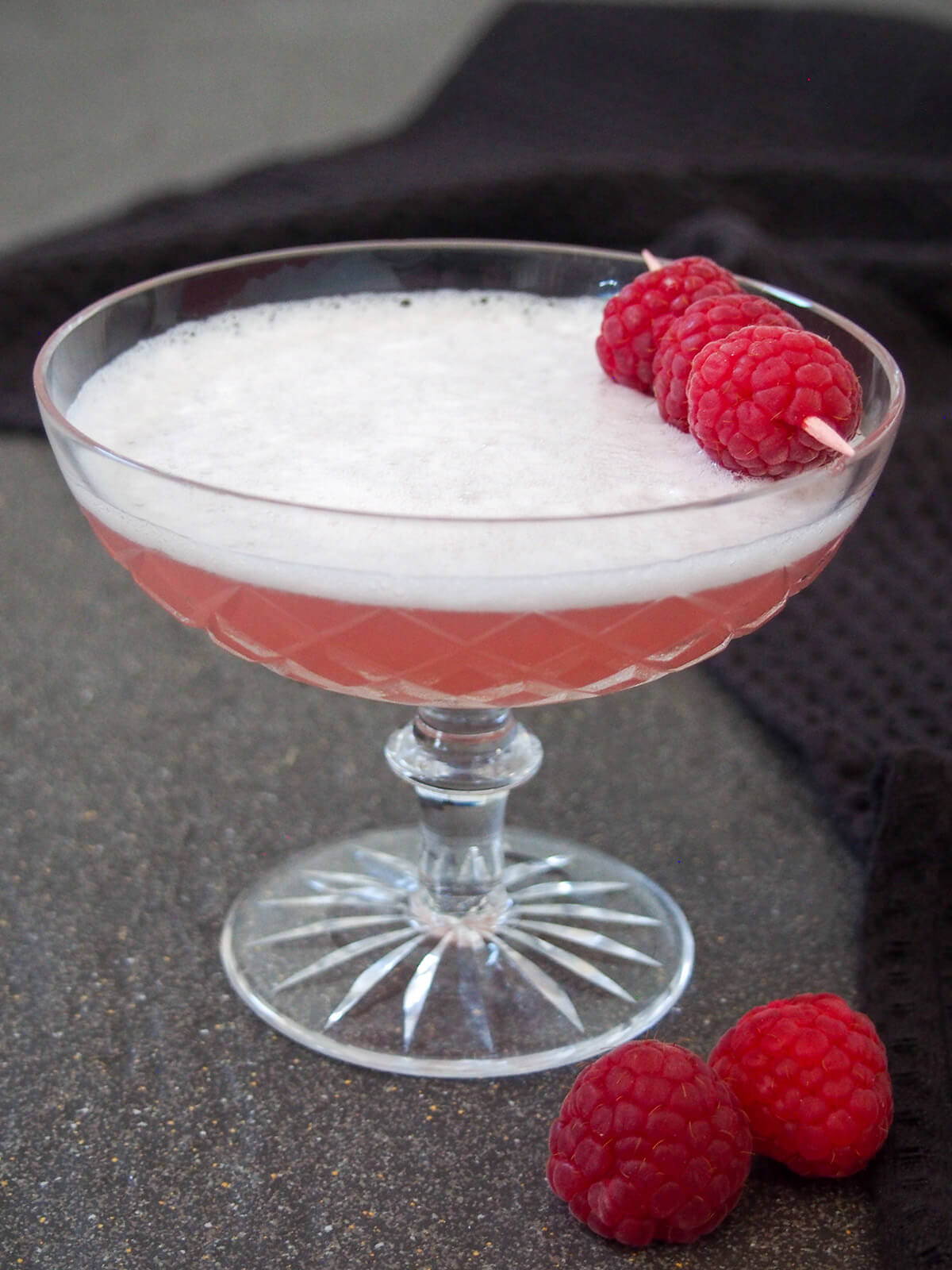glass of Clover club in Paris - a gin cocktail with raspberries on top and some to side of glass