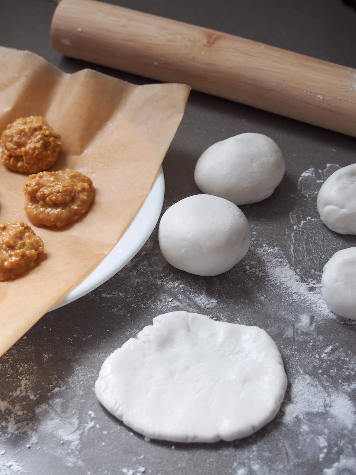 flattening out a piece of dough, other balls of dough and mounds of filling behind