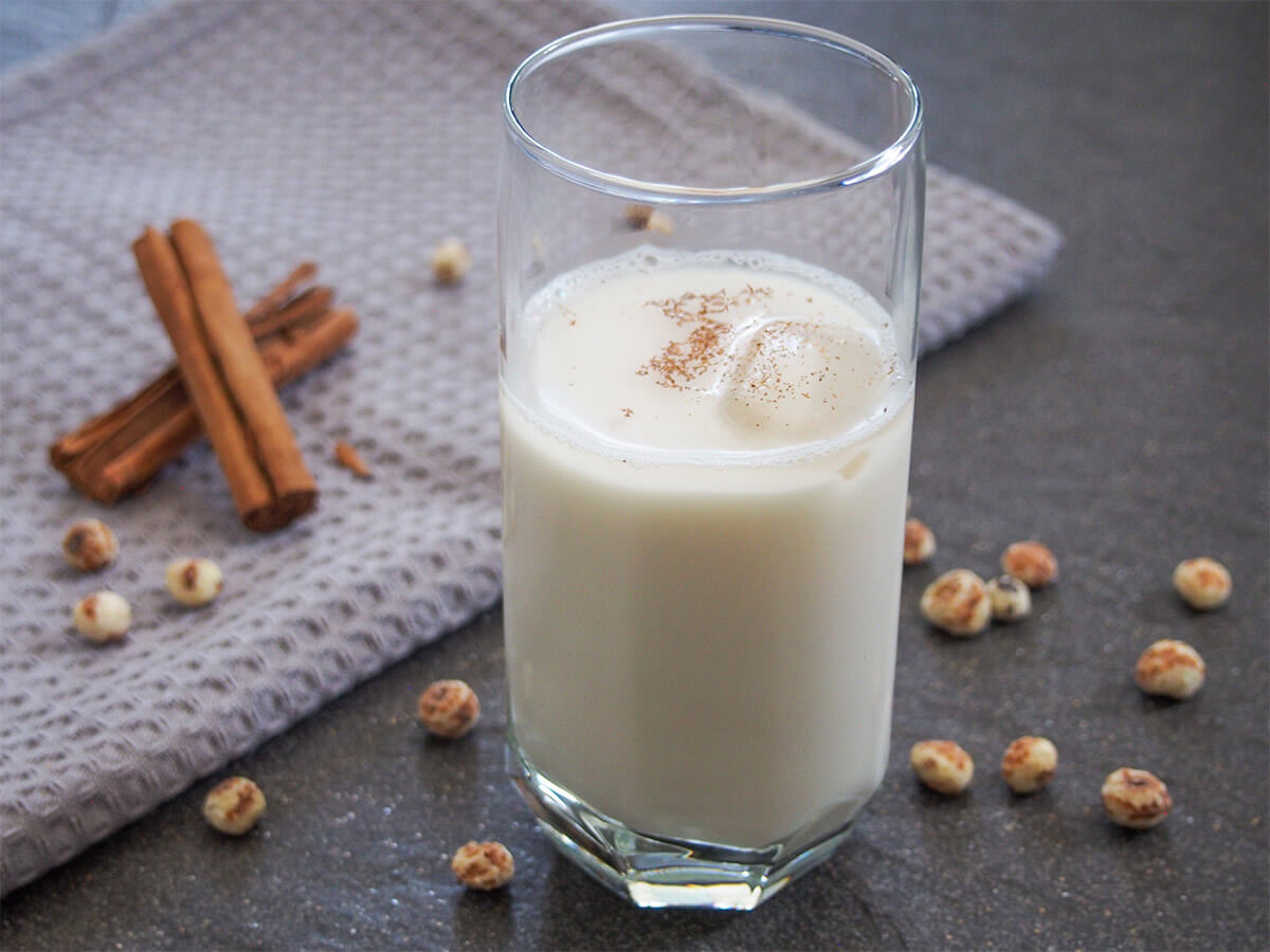 Spanish horchata de chufa made with tiger nuts is gluten free and dairy free, not to mention refreshing and delicious. Perfect for a hot day. glass of horchata de chufa with tiger nuts and cinnamon sticks behind