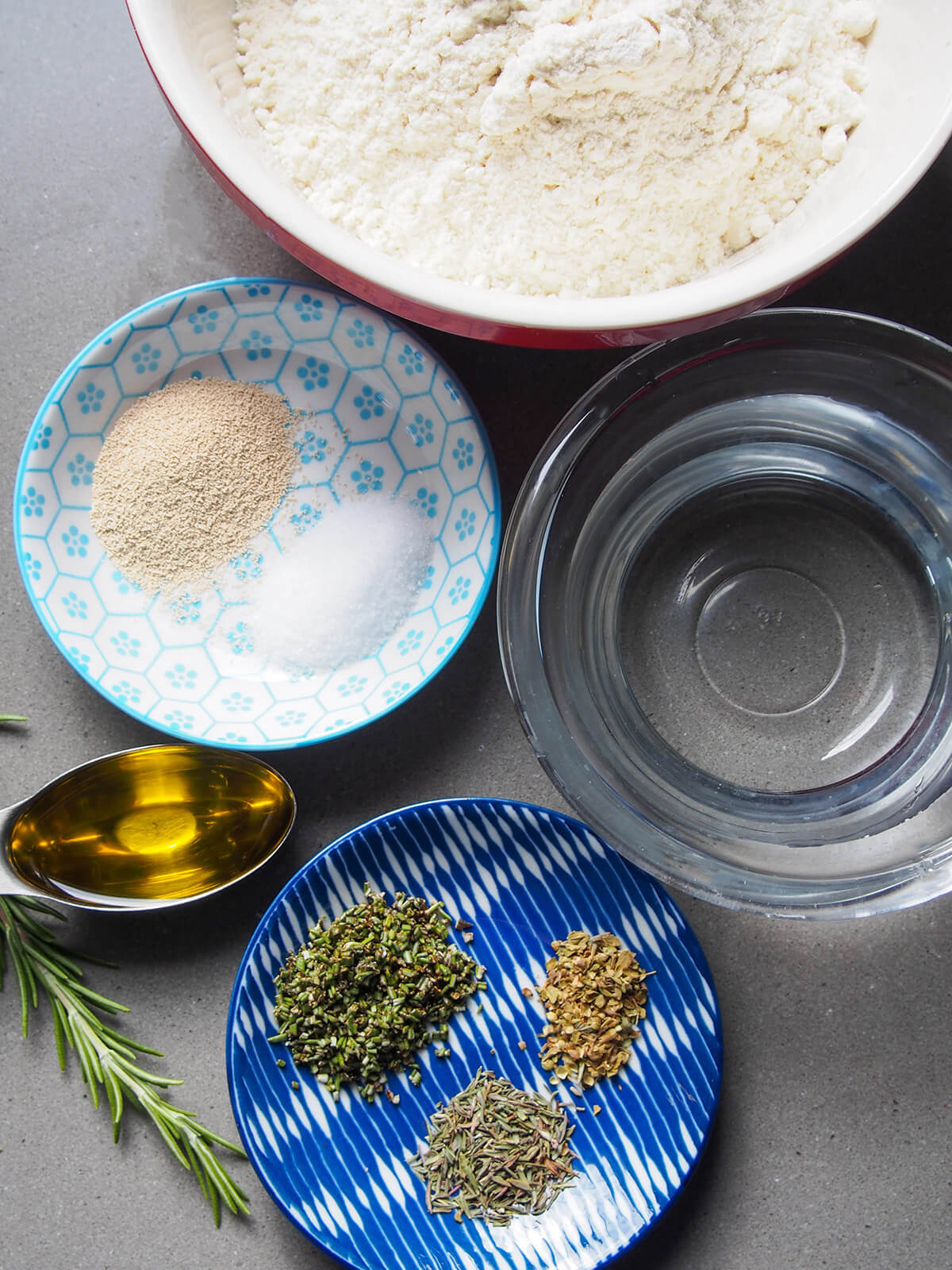 bowls with flour, water, herbs, salt and yeast plus spoon of oil