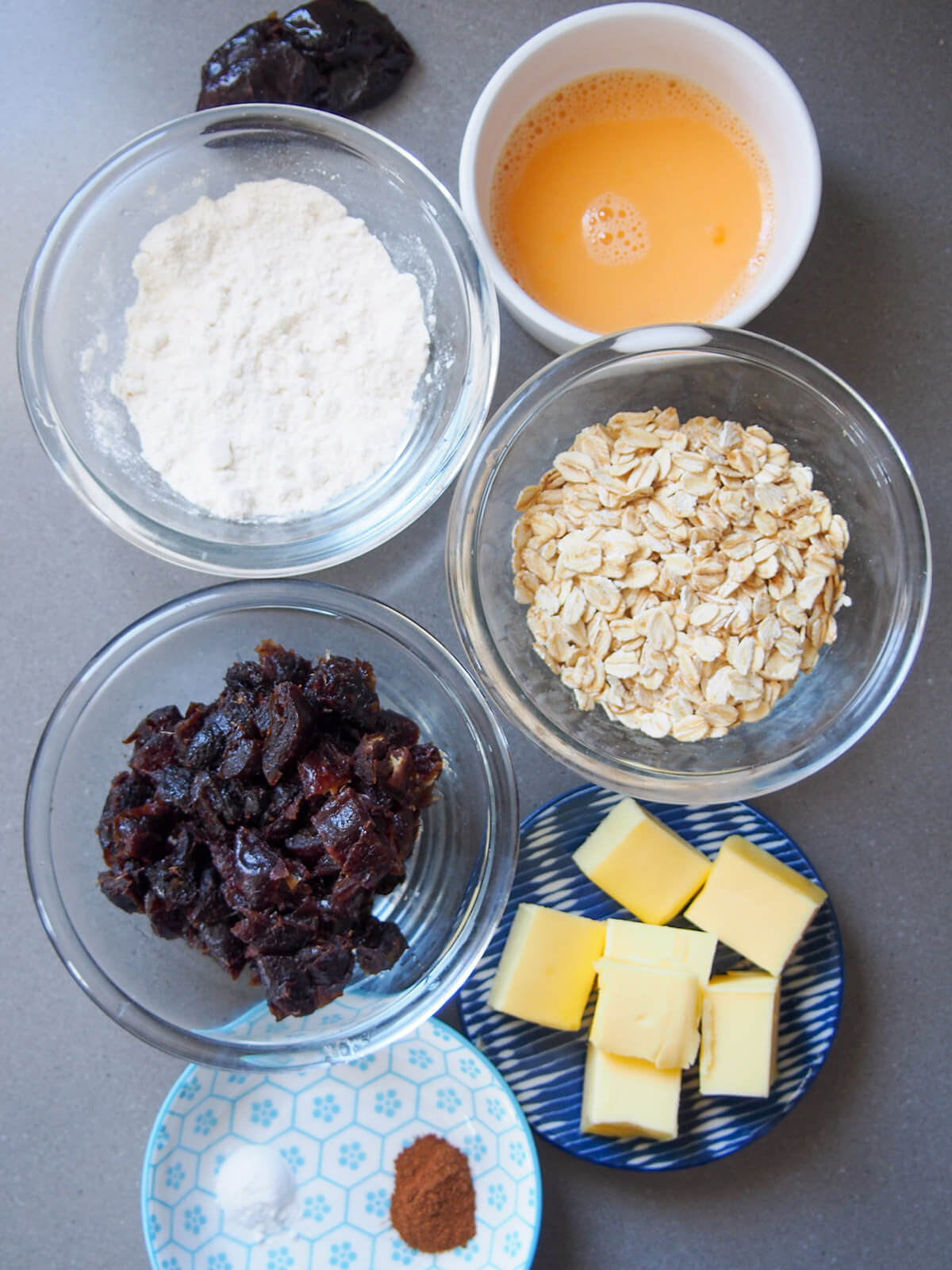 bowls with flour, oats, egg, dates, butter and plate with cinnamon and baking soda