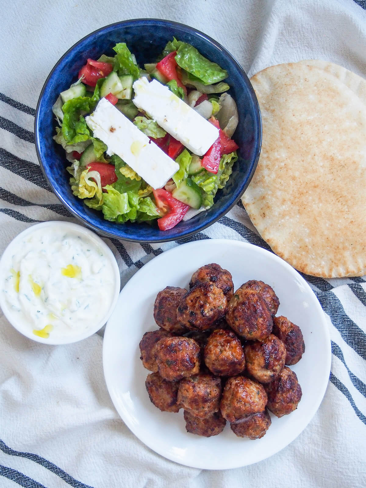 plates of keftedes, tzatziki and salad with pita to side from overhead