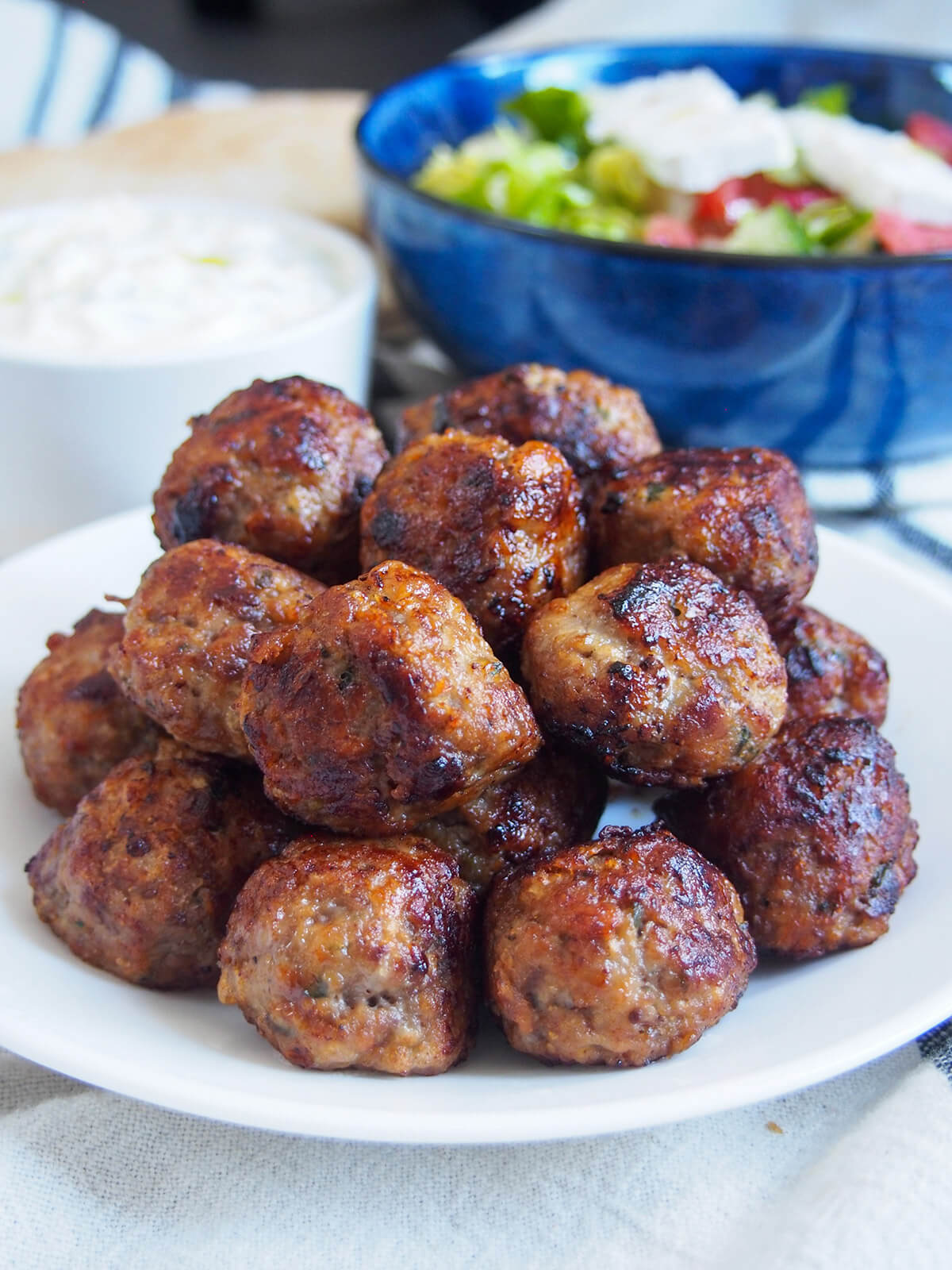 stack of keftedes Greek meatballs with bowl of salad behind