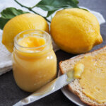 jar of lemon curd with lemons behind and toast to side