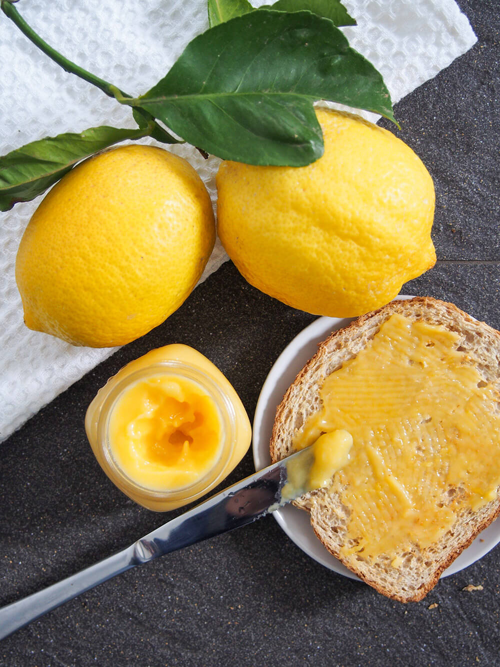 jar of lemon curd, toast with some on and lemons from overhead