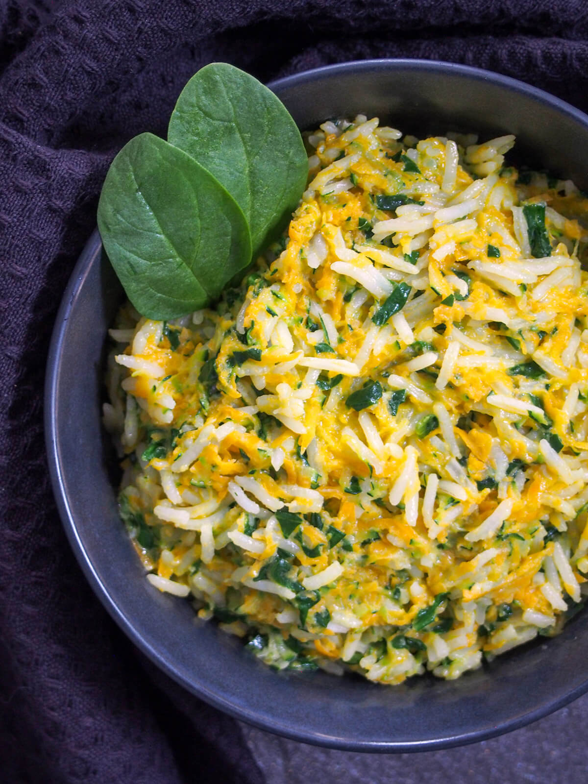 This rice with vegetables and coconut milk is extremely quick to make, using leftover rice, and makes a great side dish for a range of dishes. close up of rice with vegetables and coconut milk with spinach leaves on side of bowl