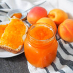 jar of apricot jam with bread and jam and fresh apricots behind