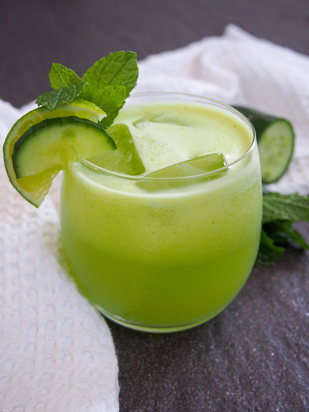 glass of cucumber agua fresca with garnishes of cucumber, lime and mint to one side