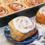 eggnog cinnamon rolls with one iced in front of dish with more