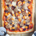 fall pizza with squash and sausage with cutter to side
