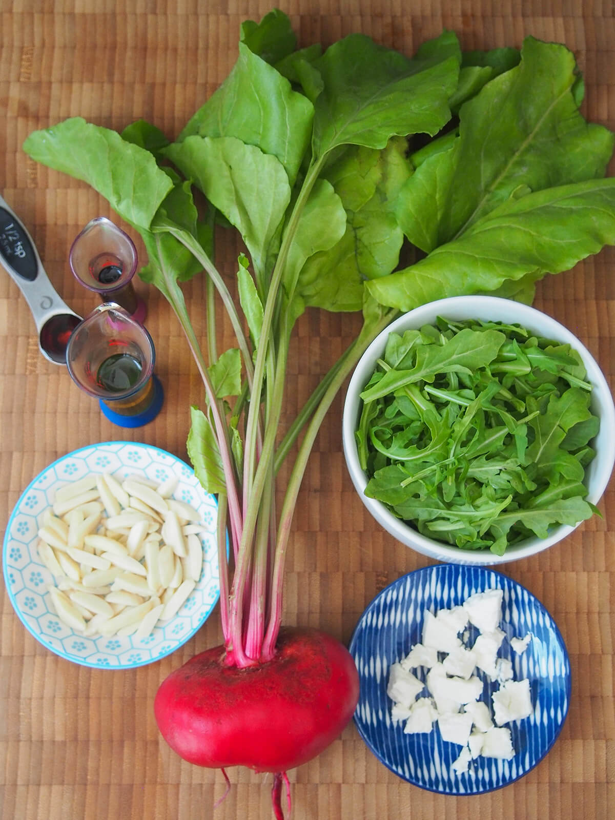 beet, bowl of arugula, some cheese on a plate and almonds on another