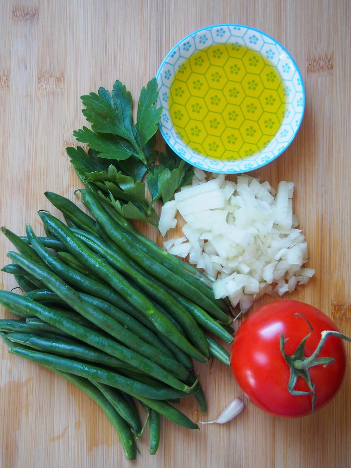 green beans, onion, tomato, olive oil and parsley on chopping board