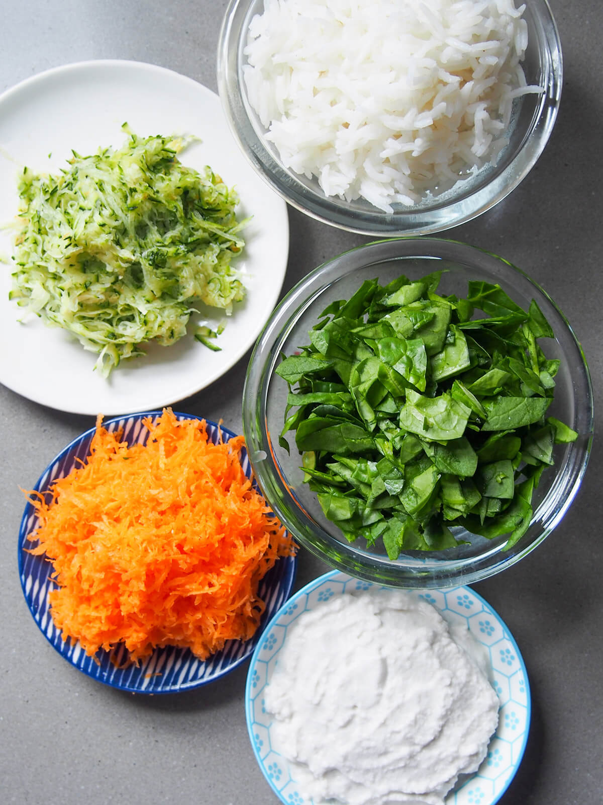 ingredients for rice with vegetables and coconut milk bowls with cooked rice, grated zucchini and carrot, spinach and coconut milk
