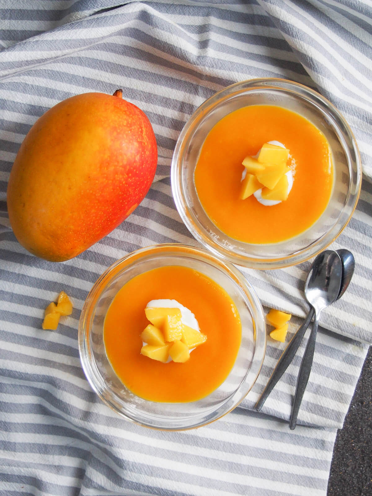 two dishes of mango panna cotta with whole mango to side from overhead