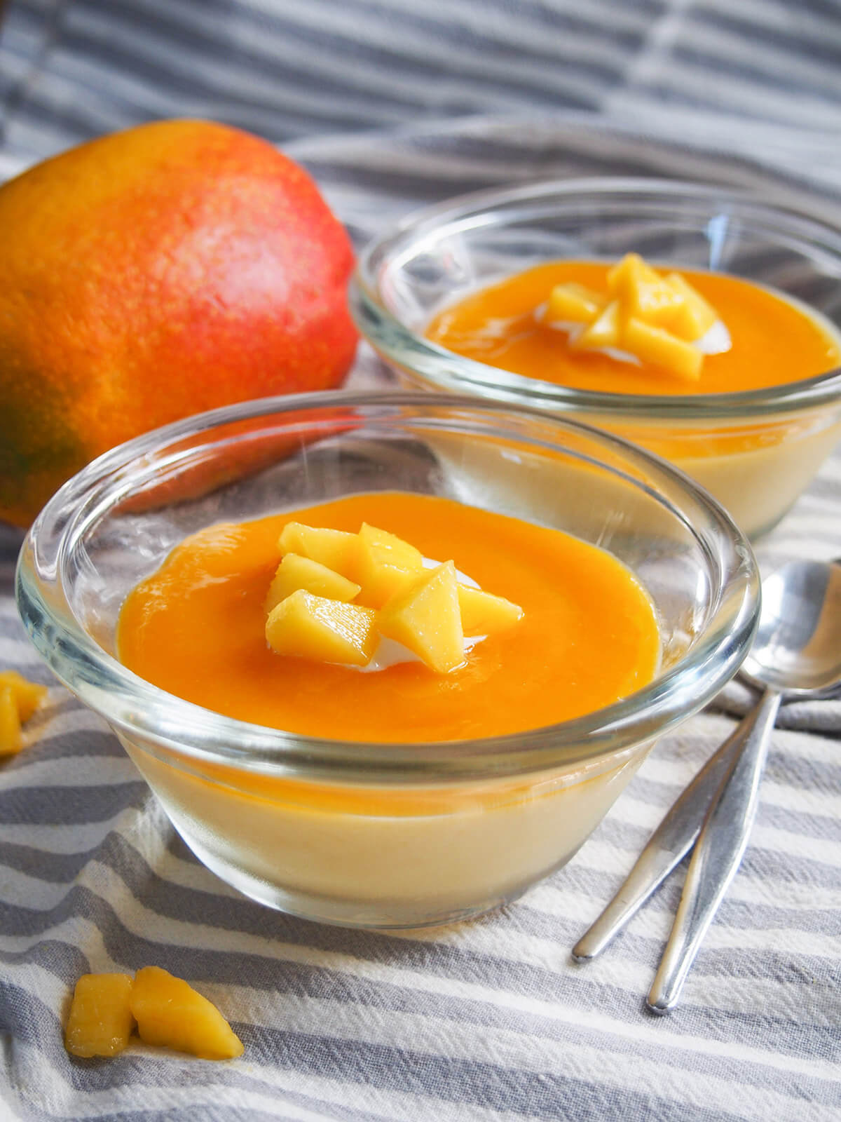two dishes of mango panna cotta with spoons to side