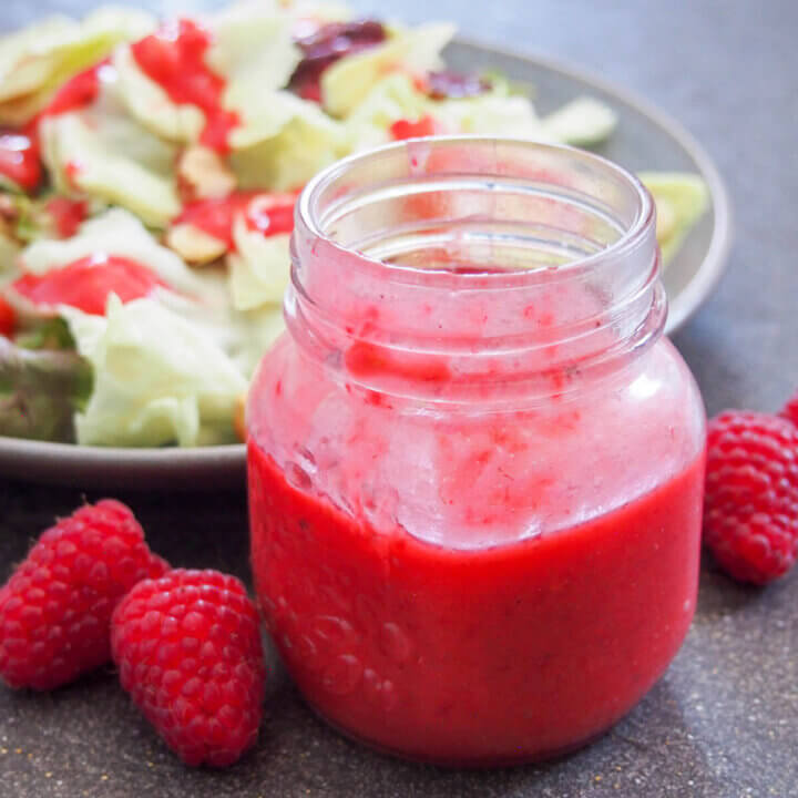 jar of raspberry vinaigrette in front of salad with some dressing on top