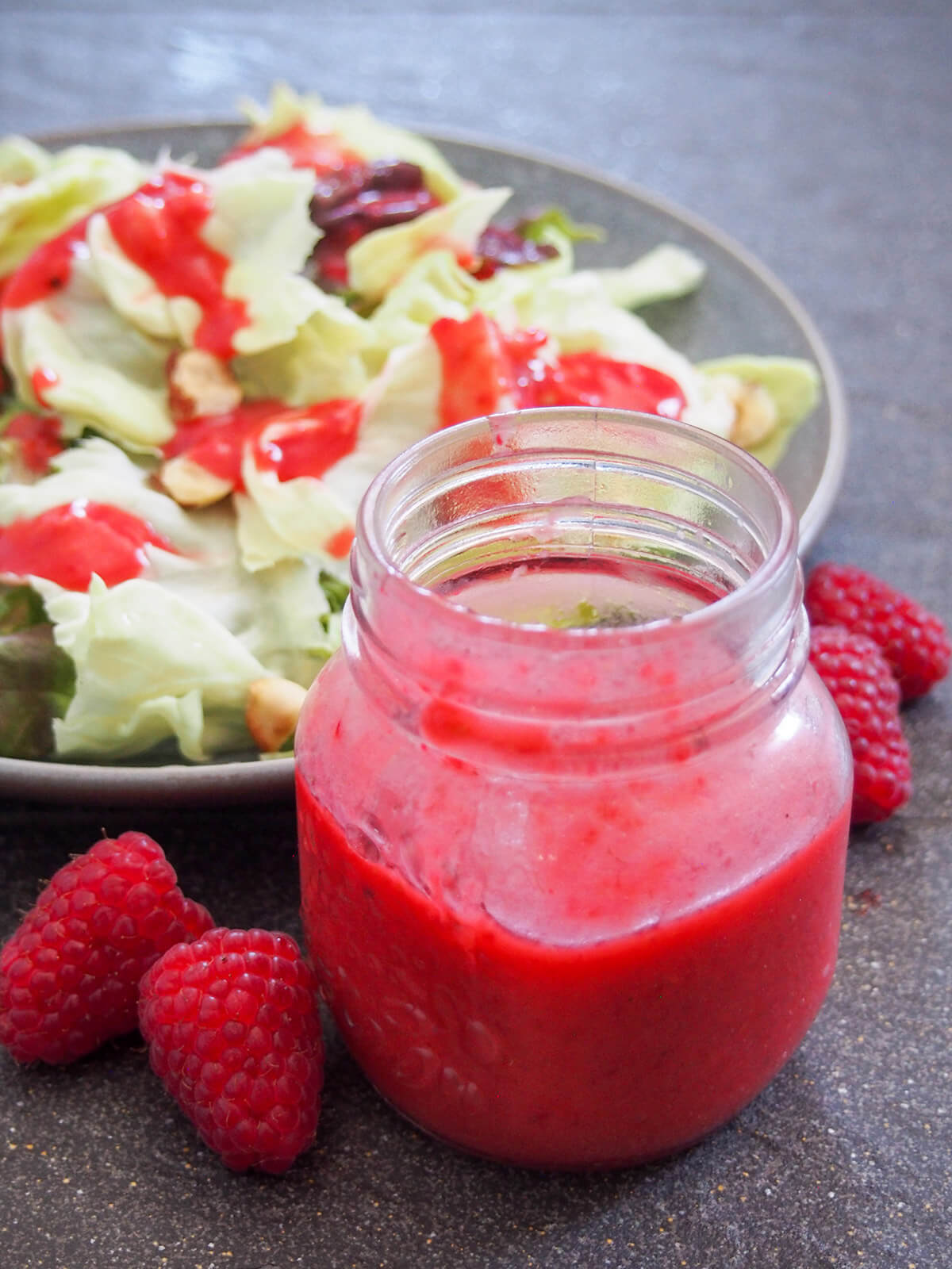 jar of raspberry vinaigrette in front of salad with some dressing on top
