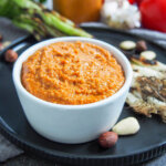 bowl of romesco sauce with nuts to side and onions behind