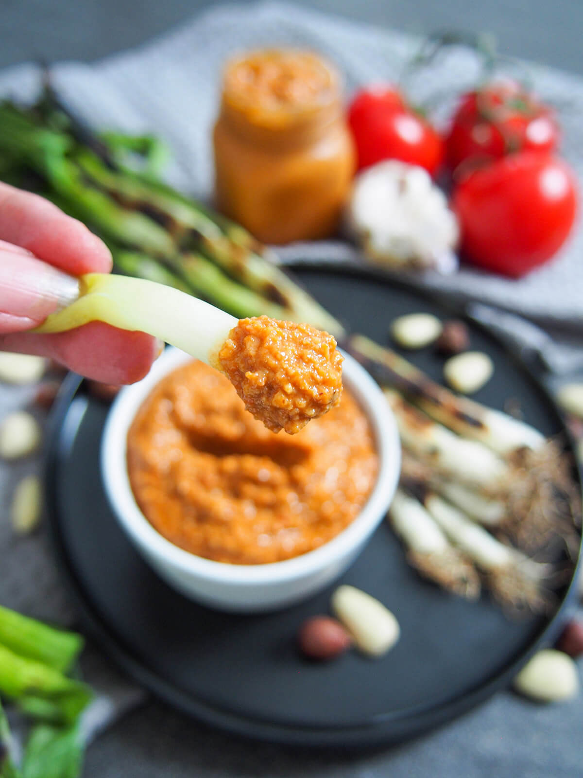 romesco sauce on a grilled spring onion held over dish with sauce and plate with grilled onions