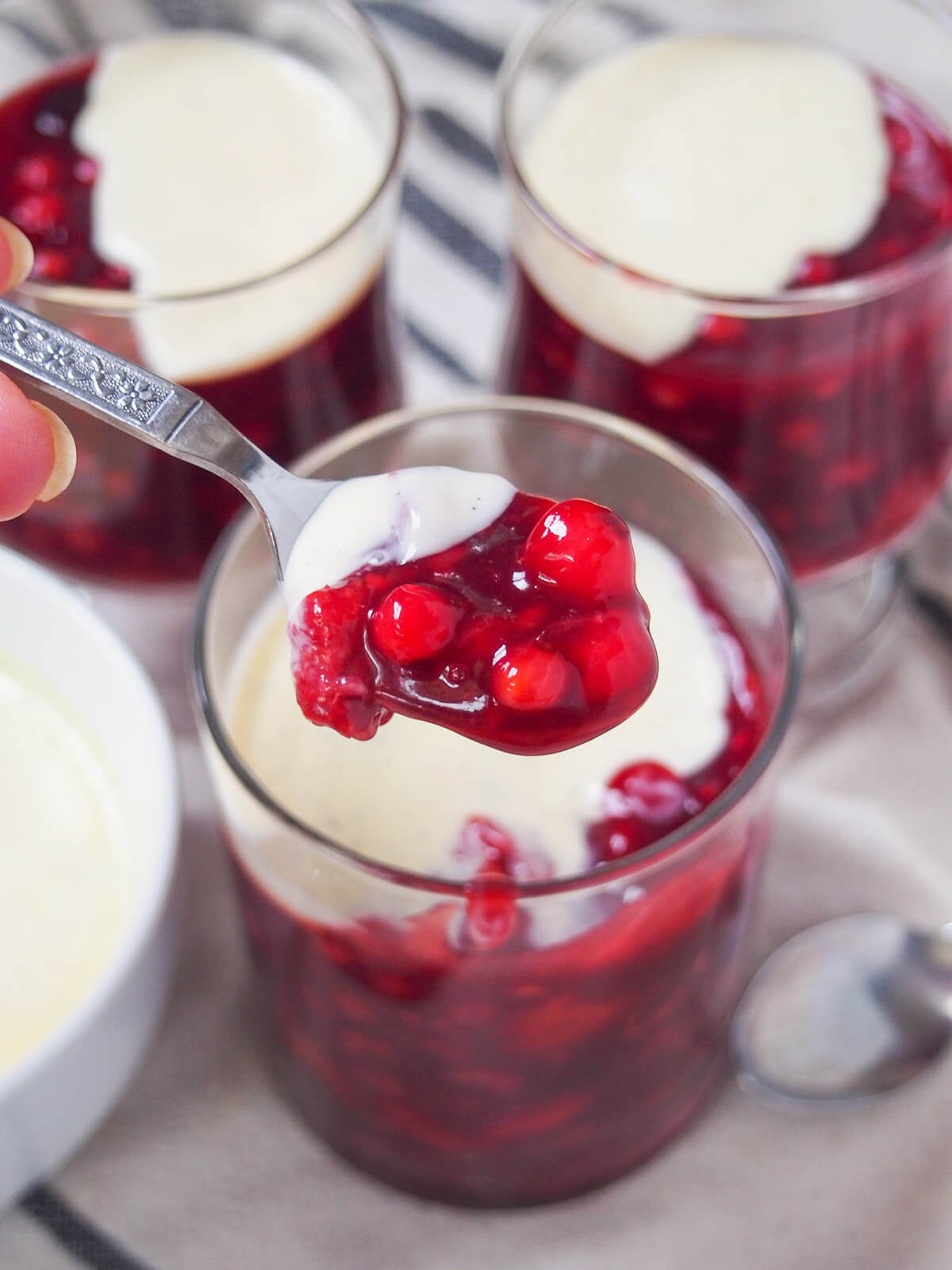 spoonful of Rote Grütze (Rote Gruetze) with vanilla sauce held over glass with more glasses in background