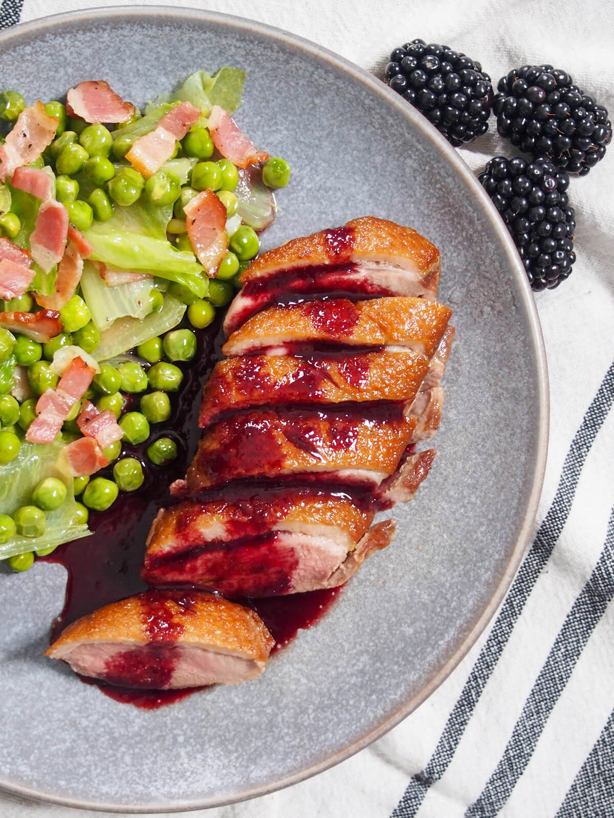 sliced pan seared duck breast with blackberry sauce from overhead with blackberries to side of plate