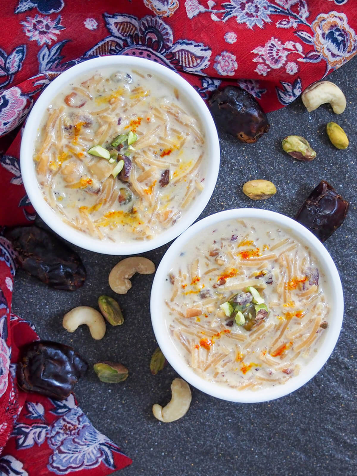 Two bowls of sheer khurma from overhead with nuts and dates to side of bowls
