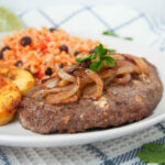 Cuban cube steak (bistec de palomilla) with onion topping and rice behind