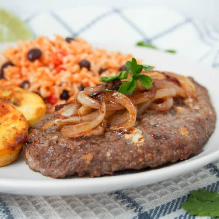 Cuban cube steak (bistec de palomilla) with onion topping and rice behind