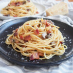 Spaghetti alla carbonara with mushrooms on black plate with a second plate in background