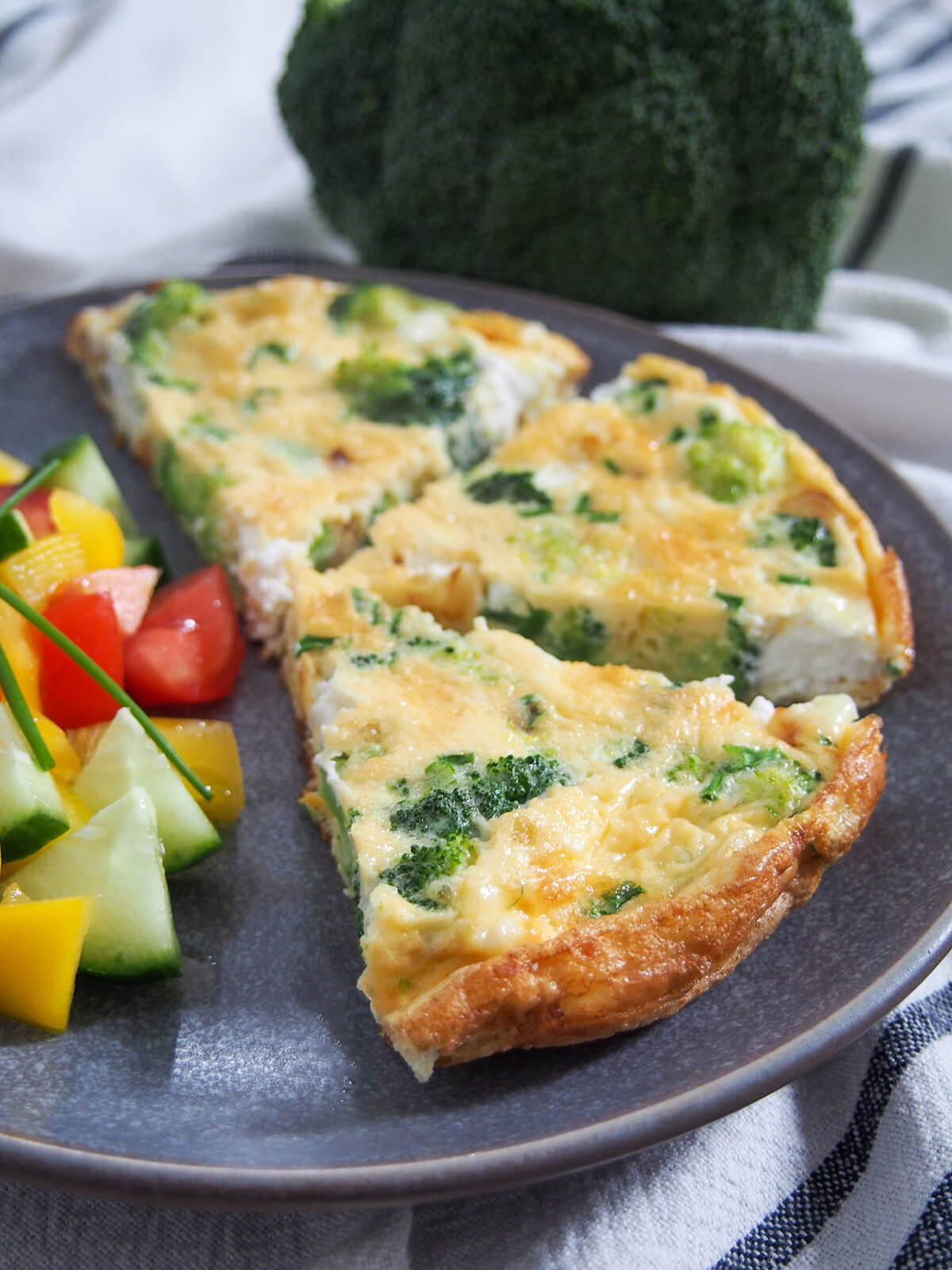 slices of broccoli goat cheese frittata with broccoli head behind plate