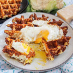 cauliflower waffle topped with egg with part cut and yolk on plate