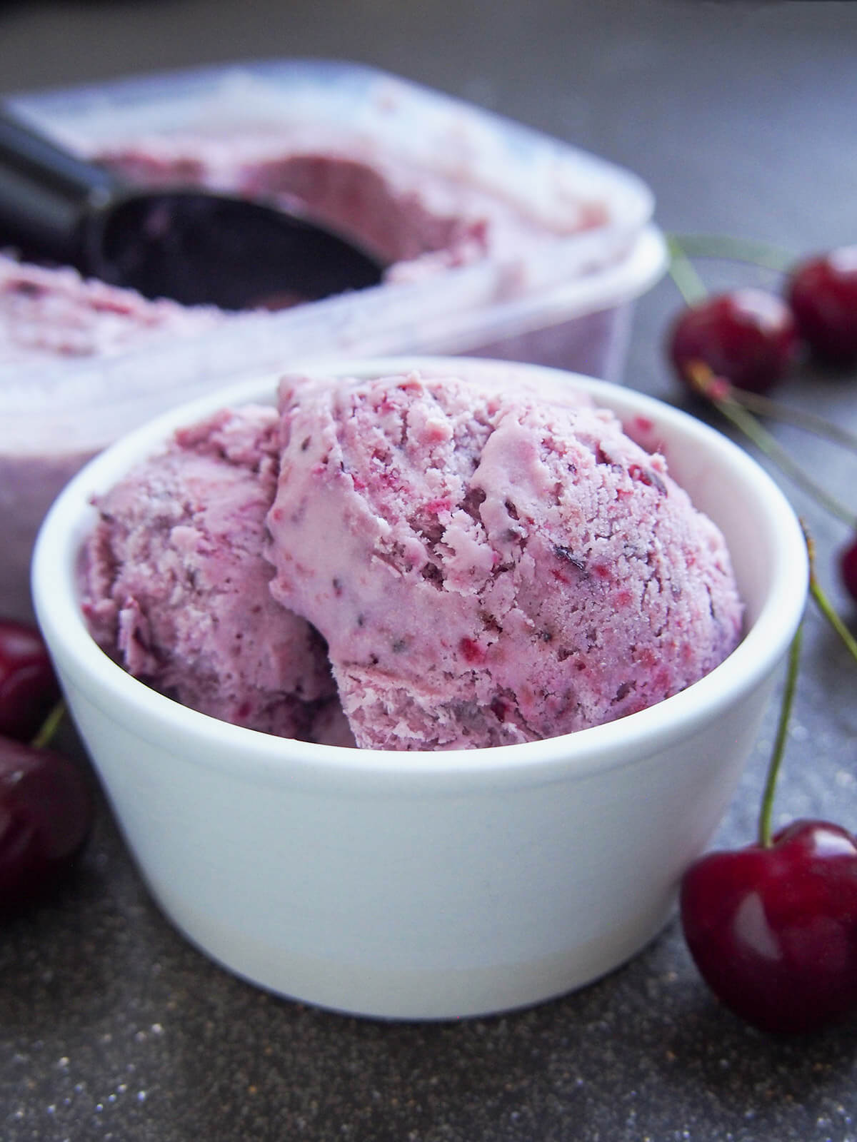 This cherry ice cream is easy to make and packed with wonderfully bright cherry flavor. It uses a simple no churn method that results in a wonderful balance of sweetness, creaminess and fruitiness. white bowl filled with cherry ice cream with tub with more behind