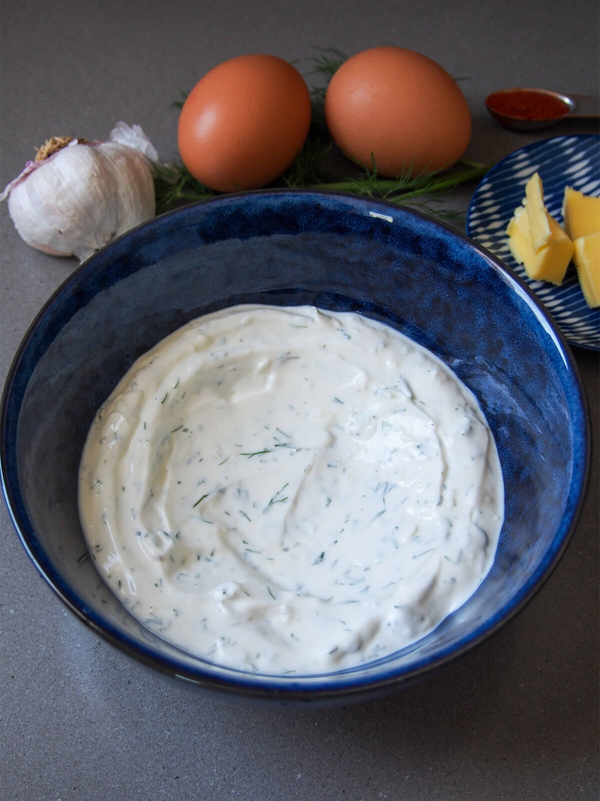 bowl with herb garlic yogurt in it with whole eggs, butter and pepper behind bowl