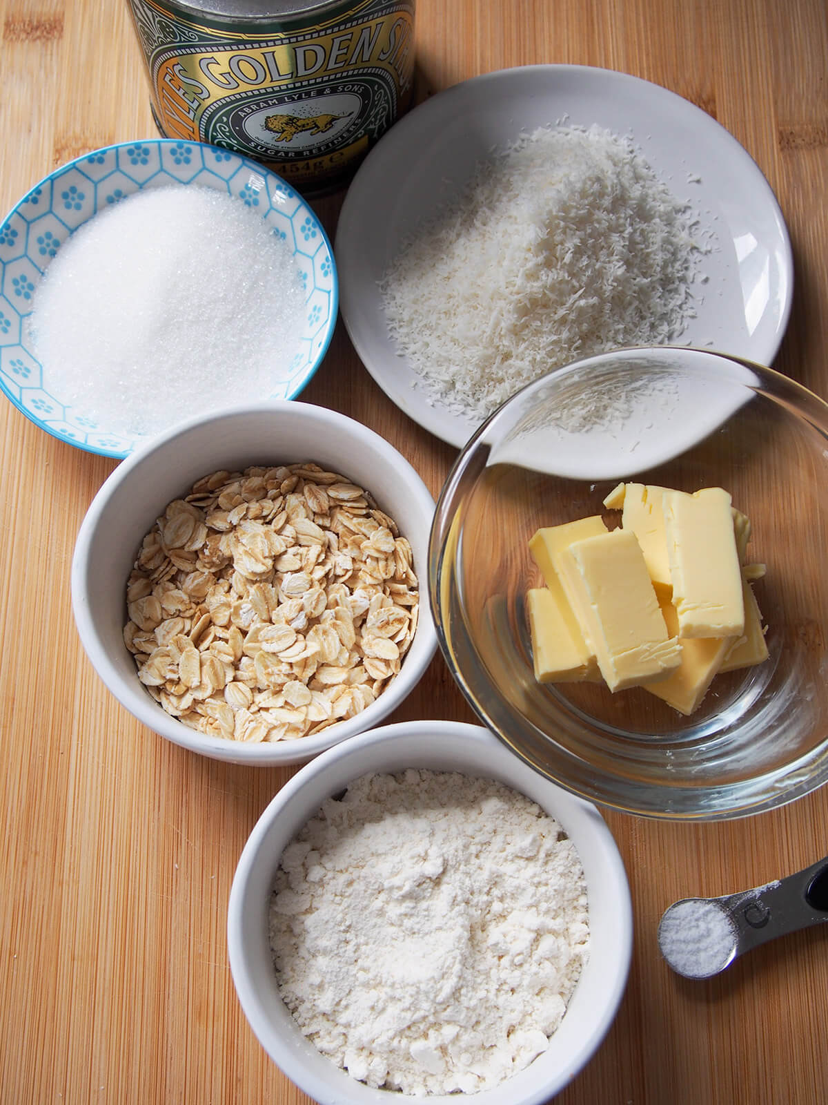 small bowls with flour, coconut, sugar, oats, butter and salt and syrup to side