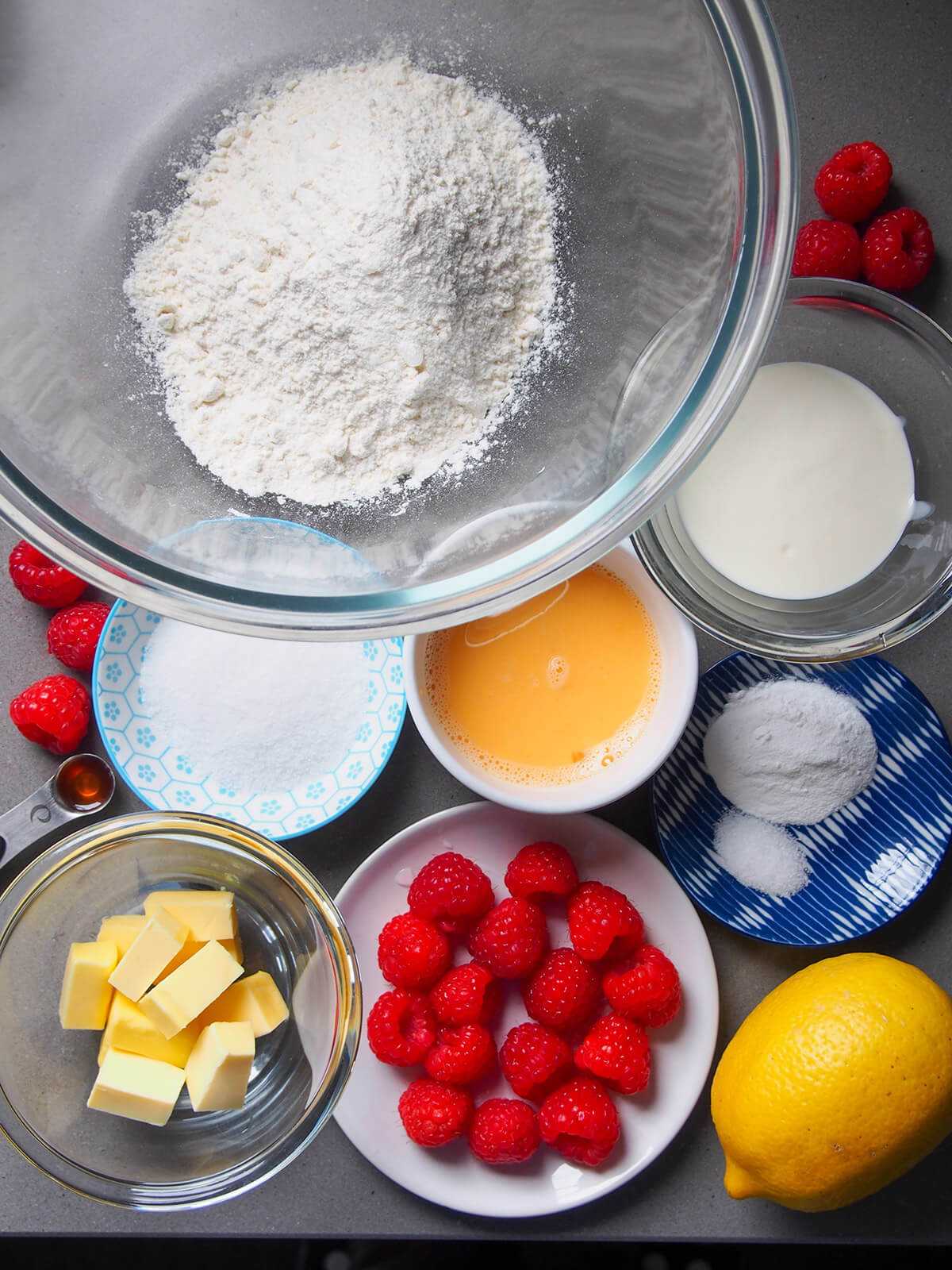big bowl of flour, smaller dishes with egg, sugar, butter, raspberries, milk and baking powder