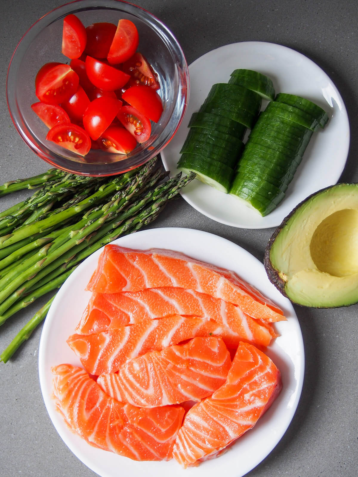 salmon, asparagus, tomatoes, cucumber and avocado in separate dishes